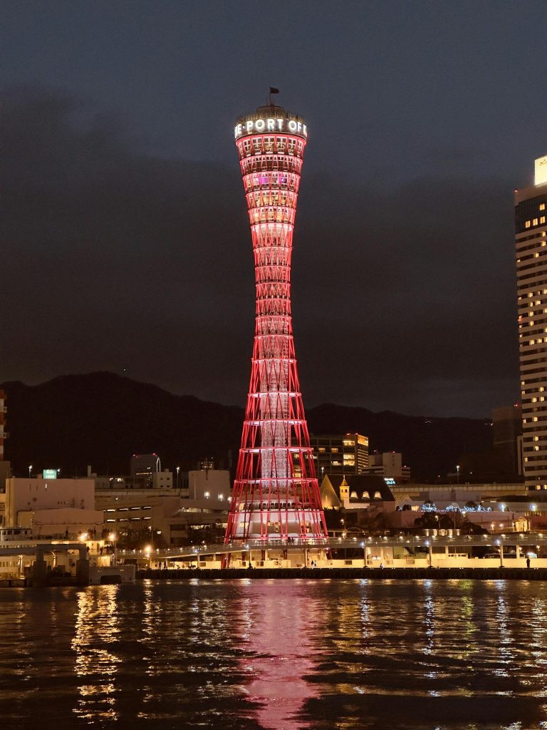 Night view of the illuminated Kobe Port Tower in Japan, reflecting on the water.