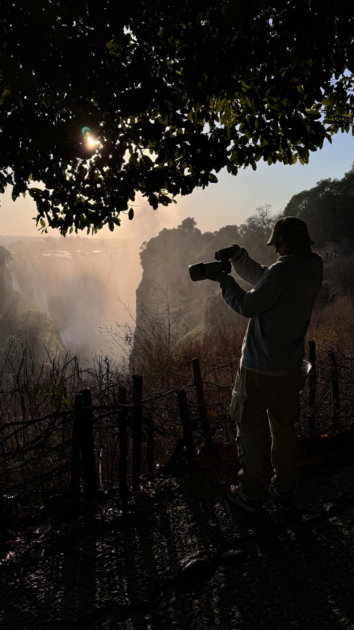 Silhouette of a photographer at sunrise capturing the majestic Victoria Falls in Zambia.
